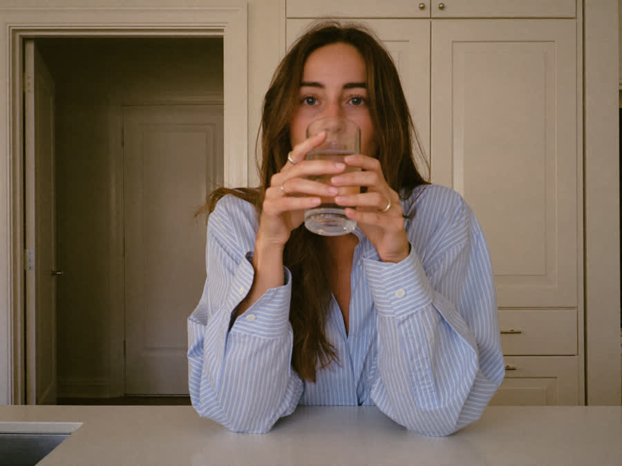 A calm woman holding a plain glass of water at her kitchen counter