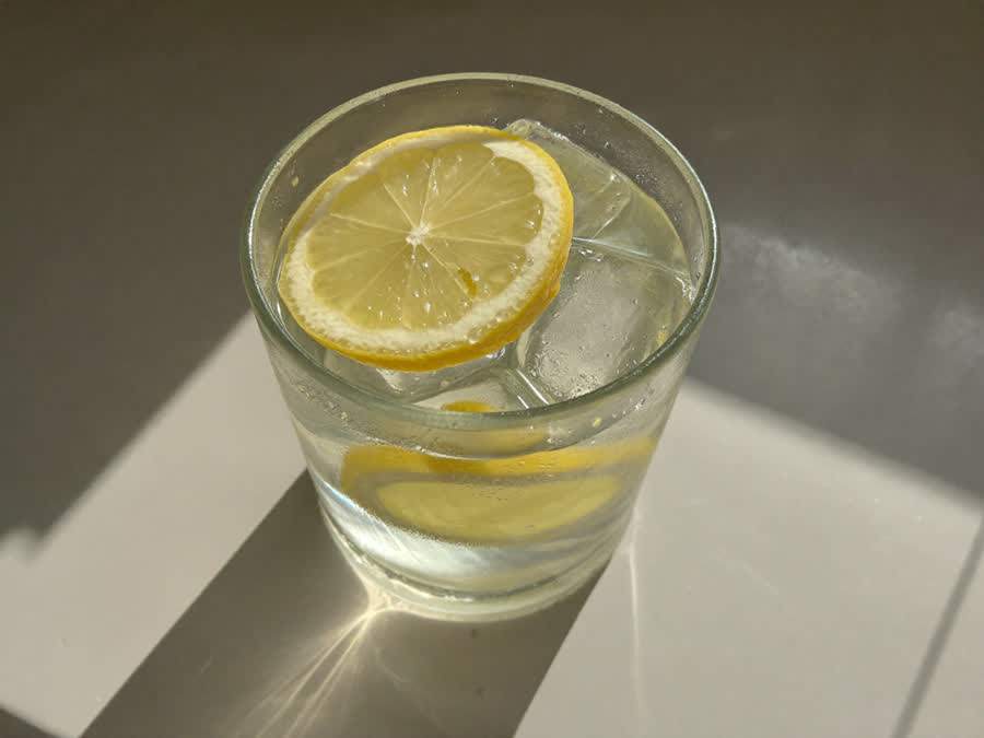 A fresh glass of lemonade with lemon and ice on a sunny counter